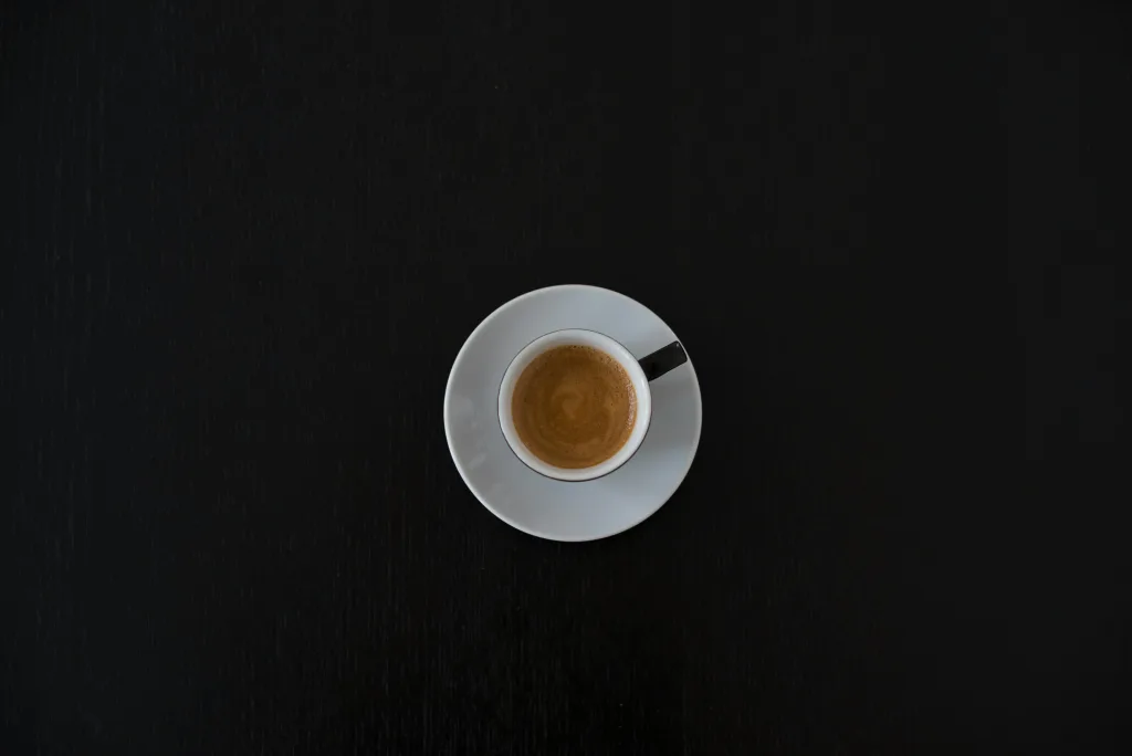 Flat lay of a white coffee cup with espresso on a black table, highlighting minimalist design.